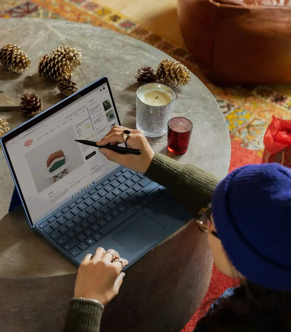 woman wearing blue beanie, pointing at a laptop screen with her pen